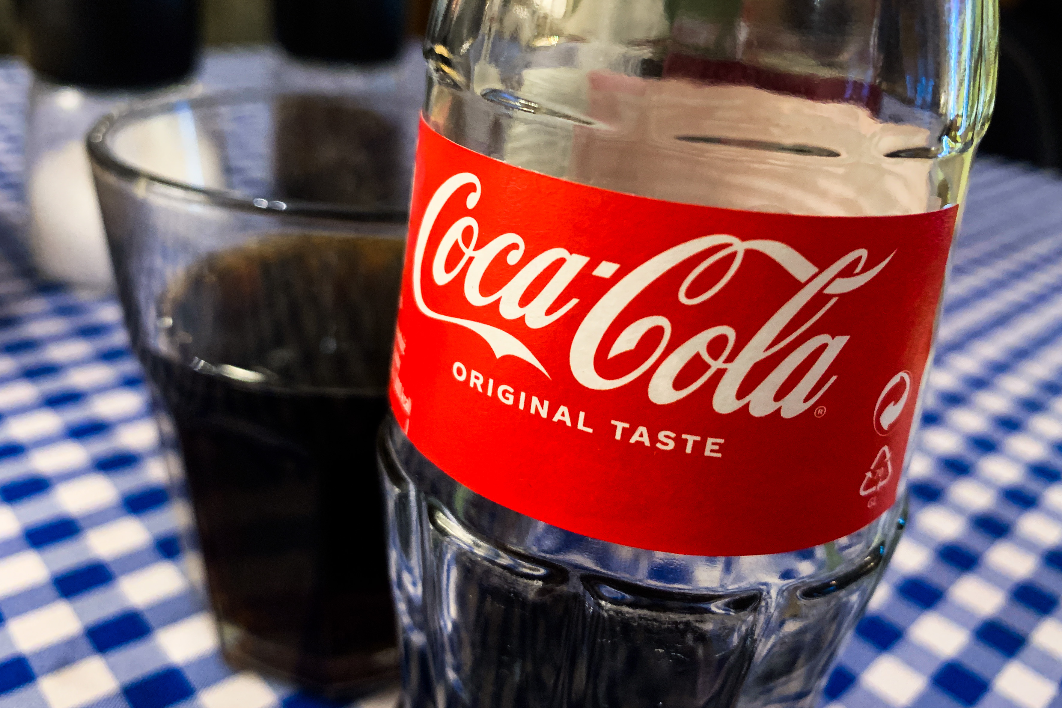 Close-up of a Coca-Cola bottle with a red label, its logo, and the phrase “Original Taste.”