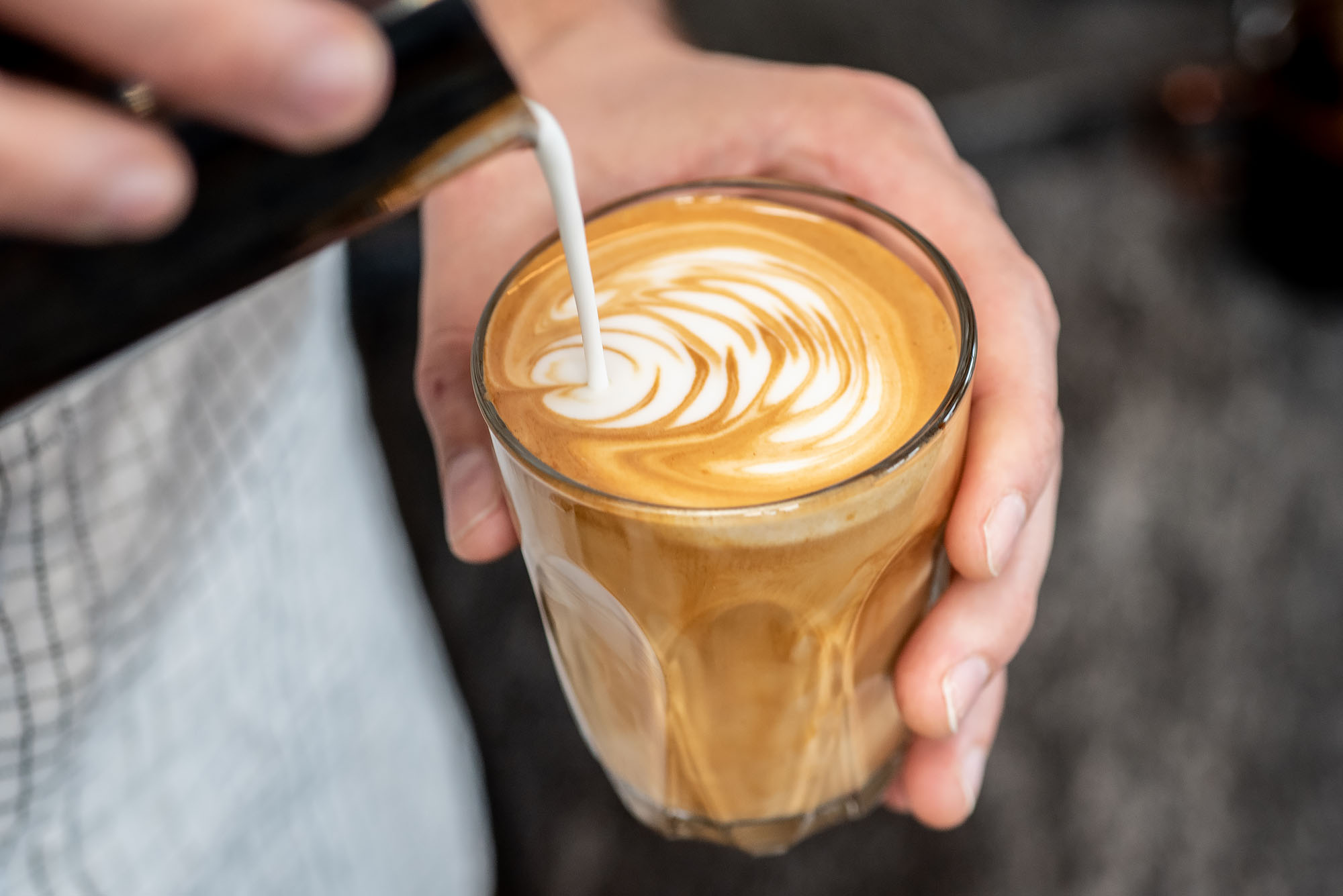 Two hands making latte art inside of a cup.