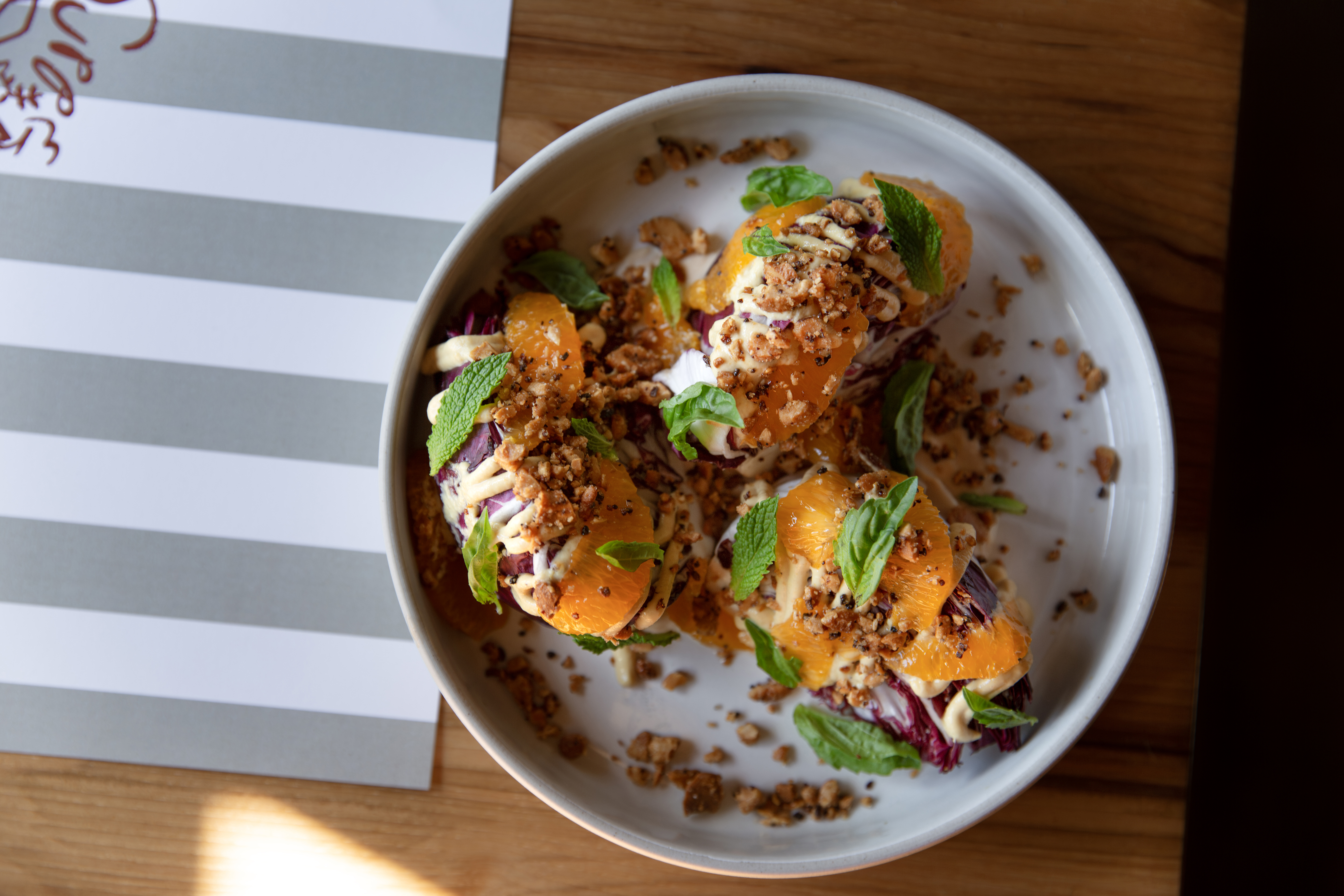 A above shot of a colorful dish of food on a round white plate on a wood surface with a white and gray surface to the left.