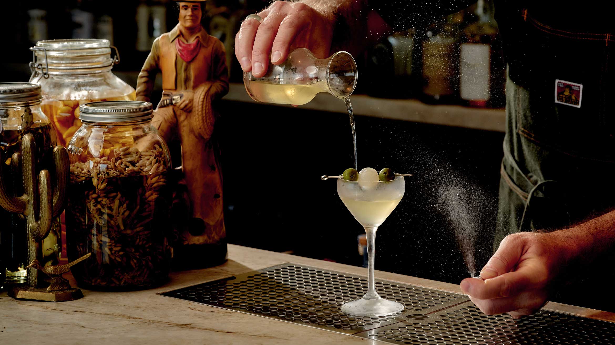 A bartender pours a drink into a cocktail glass. 